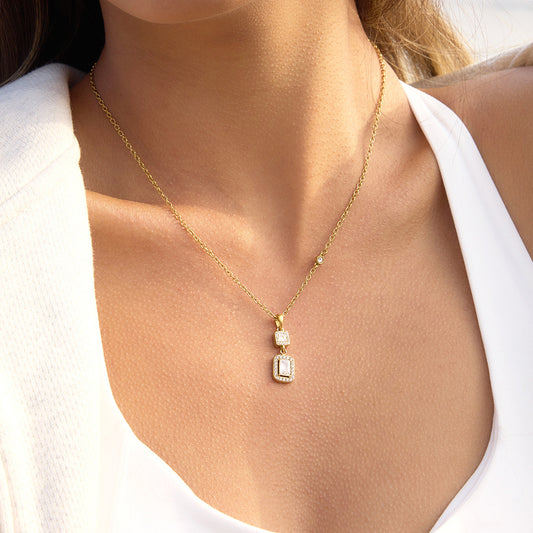 Gold necklace with diamond pendants on a person wearing a white top.