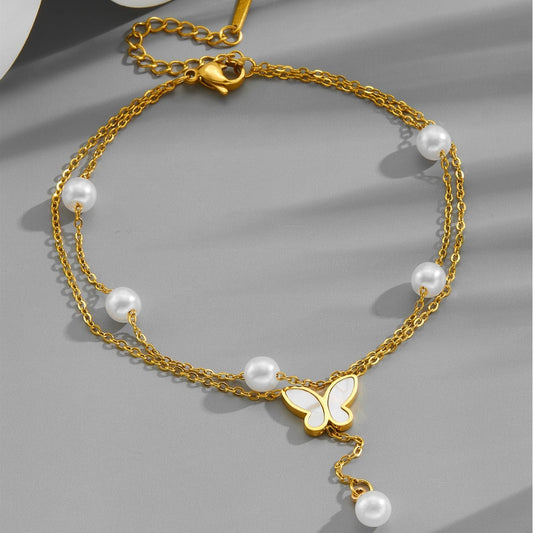 Gold anklet with pearls and a butterfly charm on a gray background