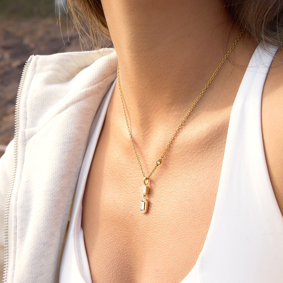 Gold necklace with a pendant on a person wearing a white top.