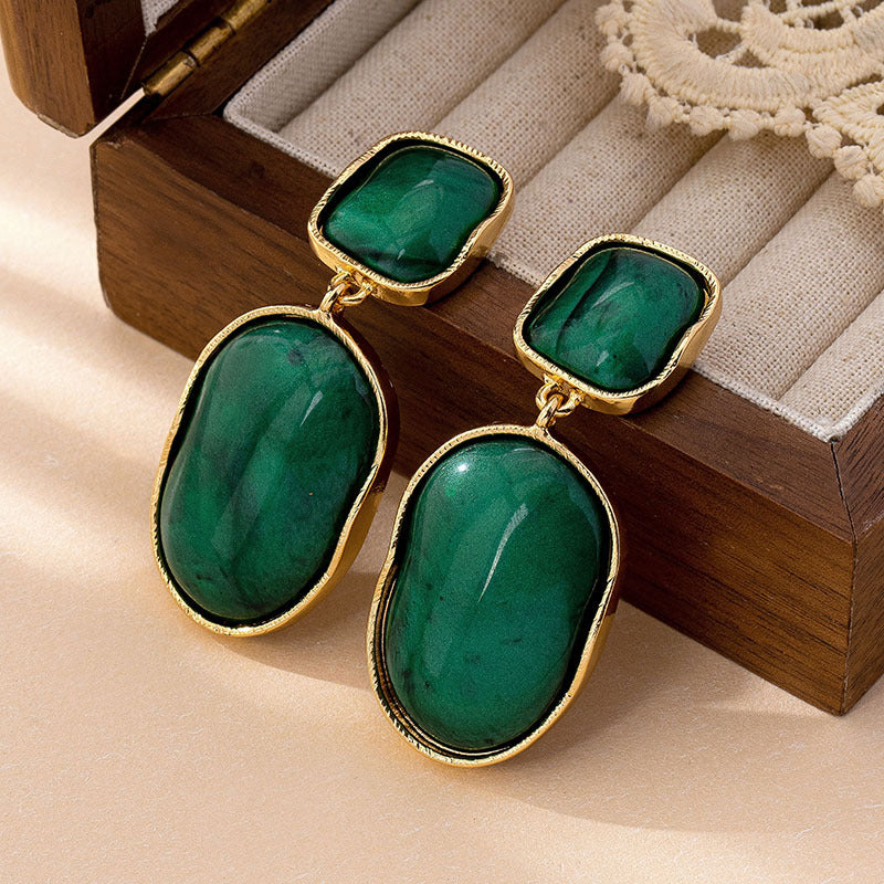 Green earrings with gold accents on a wooden surface