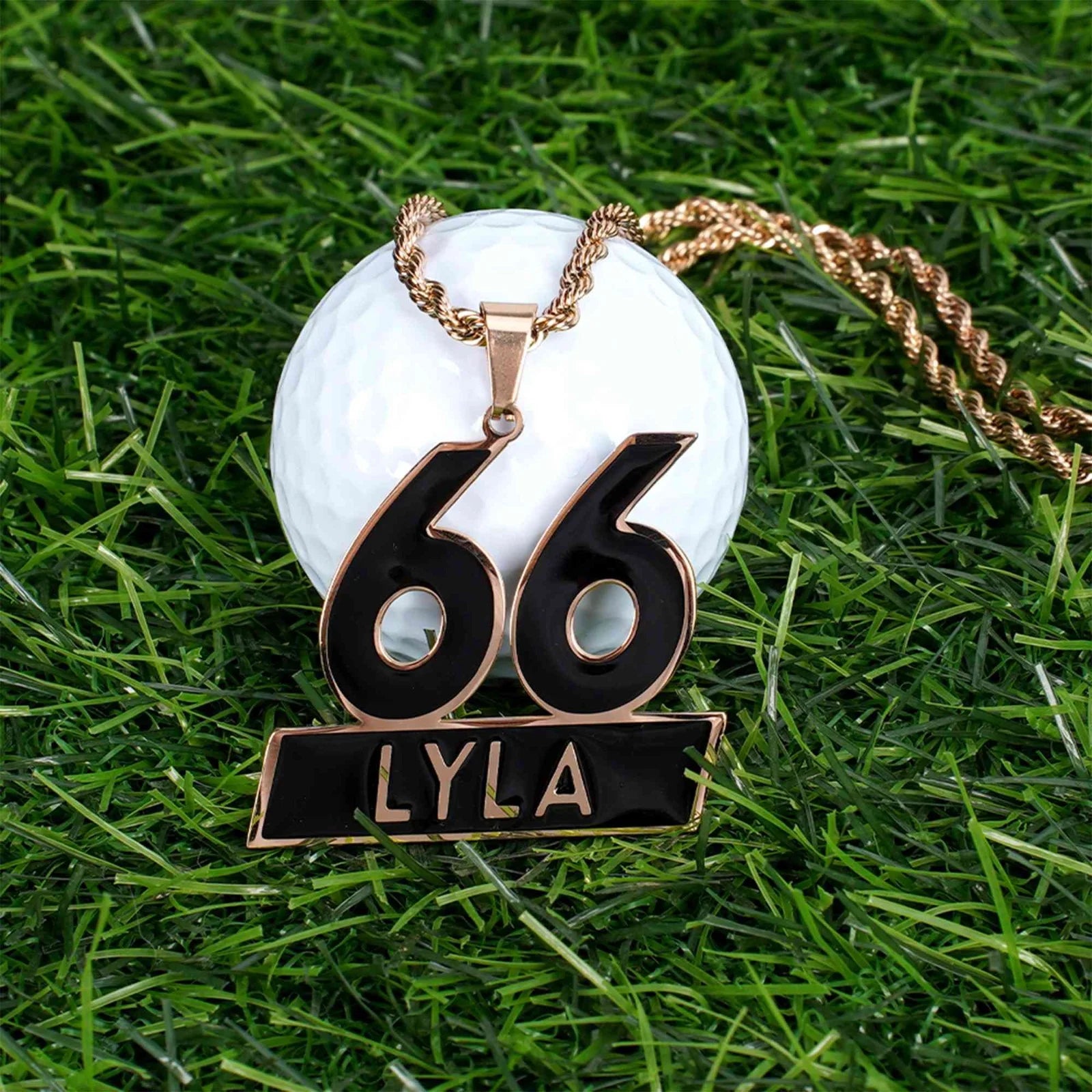 Golf ball with a necklace featuring the number 66 and name 'LYLA' on grass