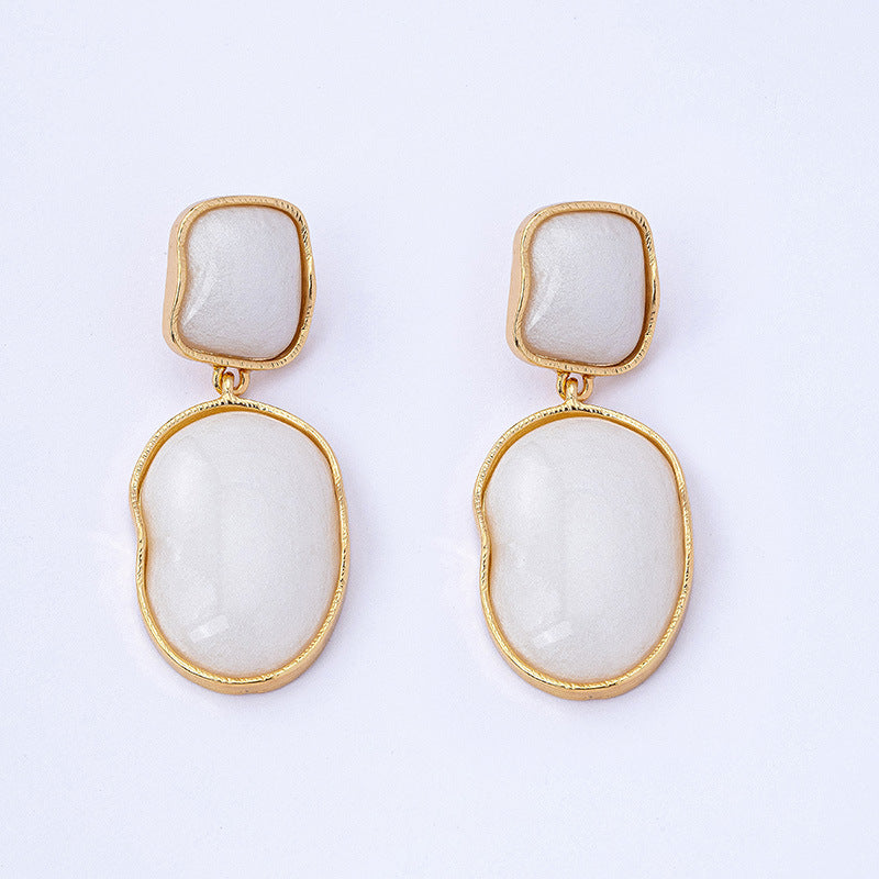 Pair of earrings with gold frames and white stone centers on a light gray background