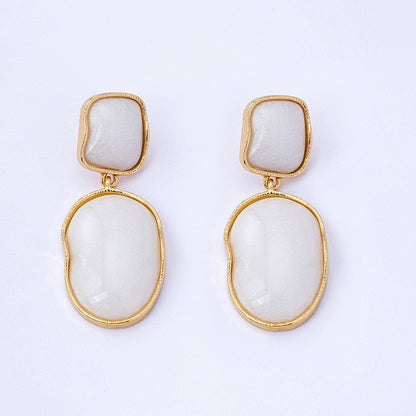 Pair of earrings with gold frames and white stone centers on a light gray background