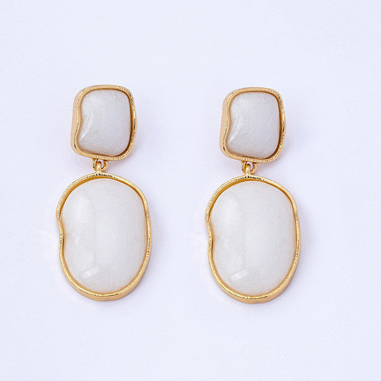 Pair of earrings with gold frames and white stone centers on a light gray background