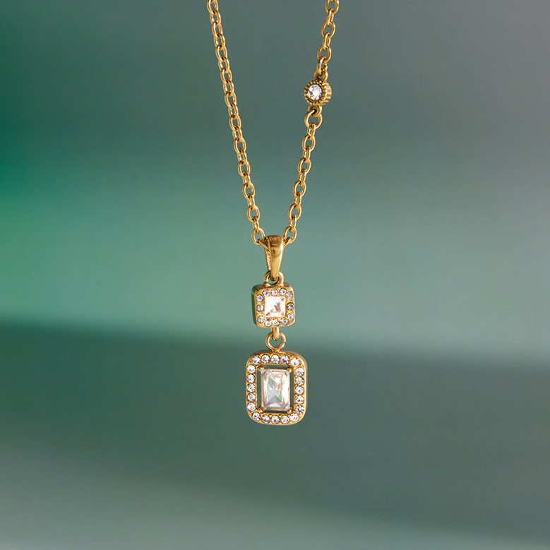 Gold necklace with two square pendant charms on a green background