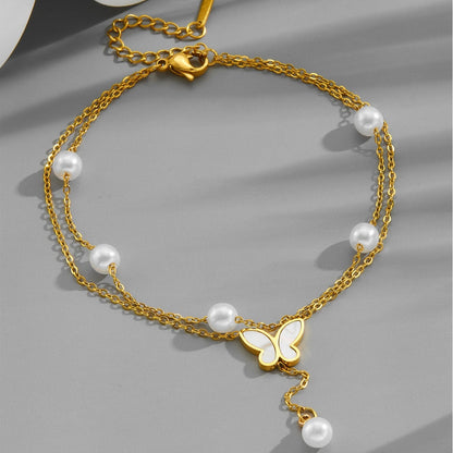 Gold anklet with pearls and a butterfly charm on a gray background