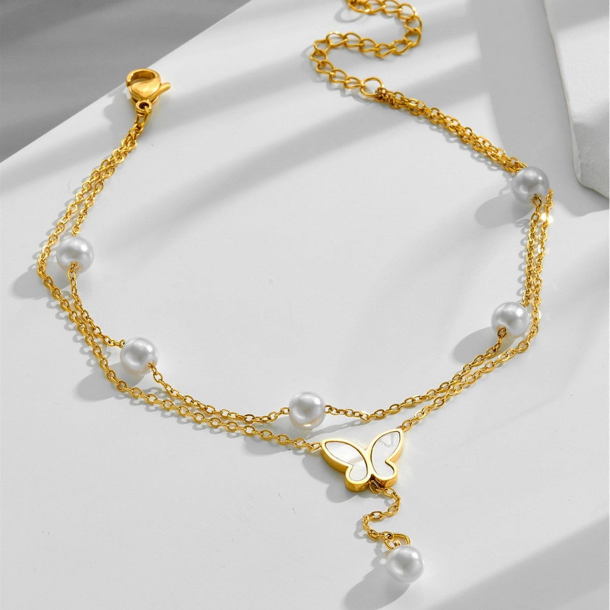 Gold anklet with pearls and a butterfly pendant on a white surface