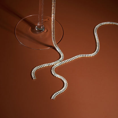 Silver snake-shaped necklace on a brown surface