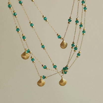 Necklace with gold shell pendants and green beads on a beige background