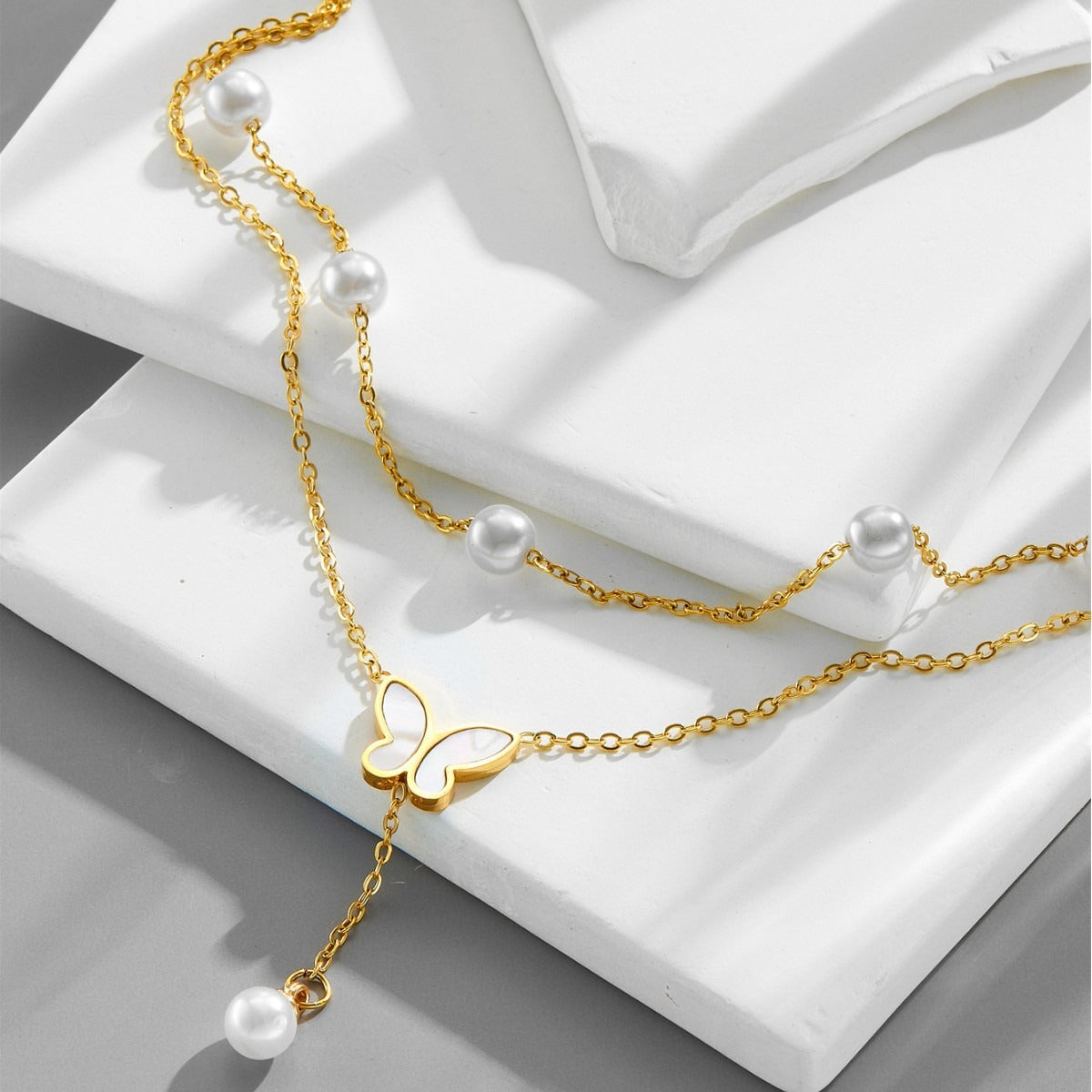 Gold anklet with butterfly pendant and pearls on a white surface