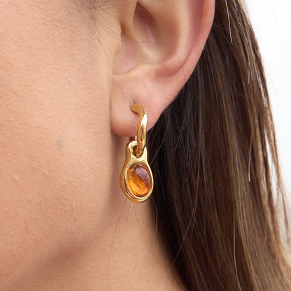 Gold earring with a amber stone worn by a person