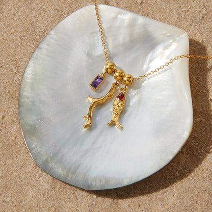 Gold necklace with charms on a shell against a sandy background