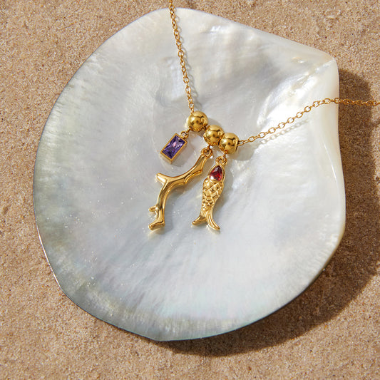 Gold necklace with charms on a shell against a sandy background