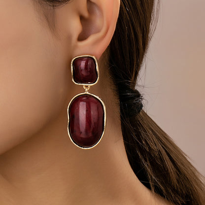 Close-up of a woman wearing burgundy earrings with gold accents.