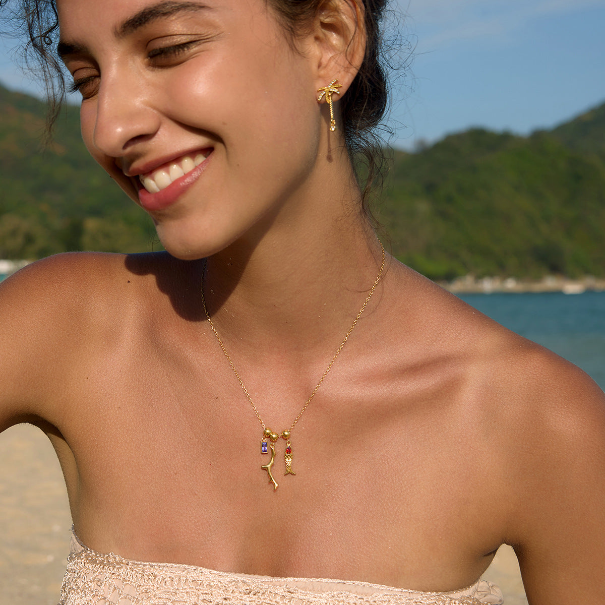 Woman on a beach wearing gold jewelry with a scenic background