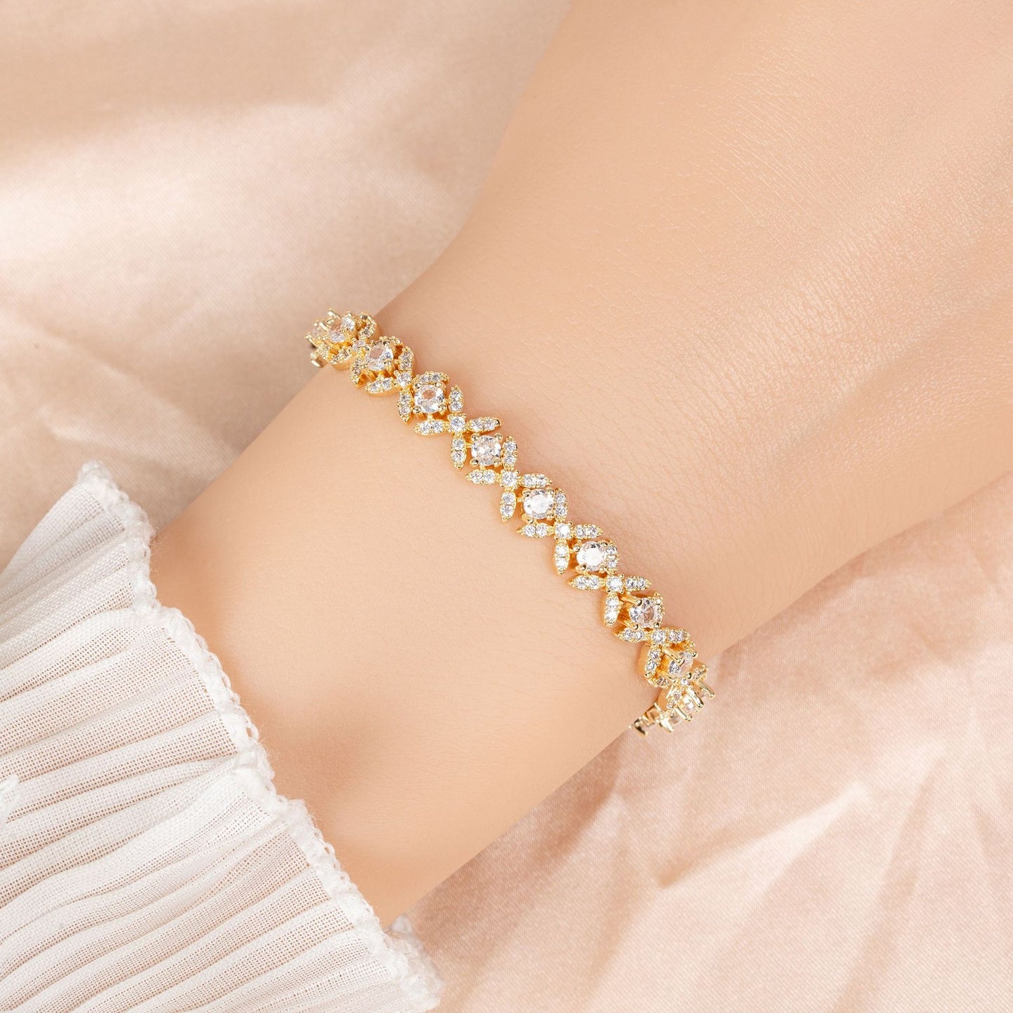 Gold bracelet with clear stones on a wrist against a soft pink background