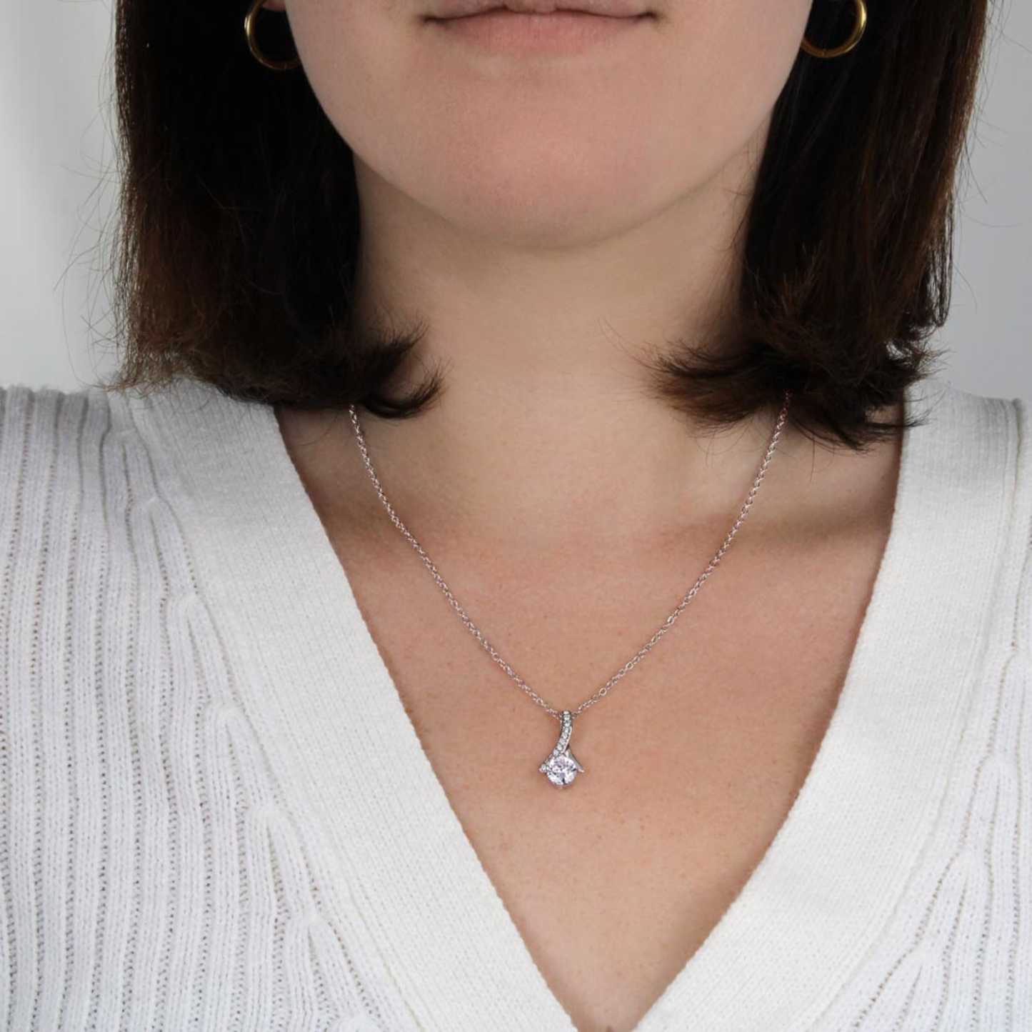 Close-up of a person wearing a silver necklace with a pendant on a plain background