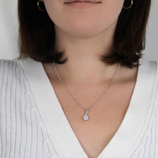 Close-up of a person wearing a silver necklace with a pendant on a plain background
