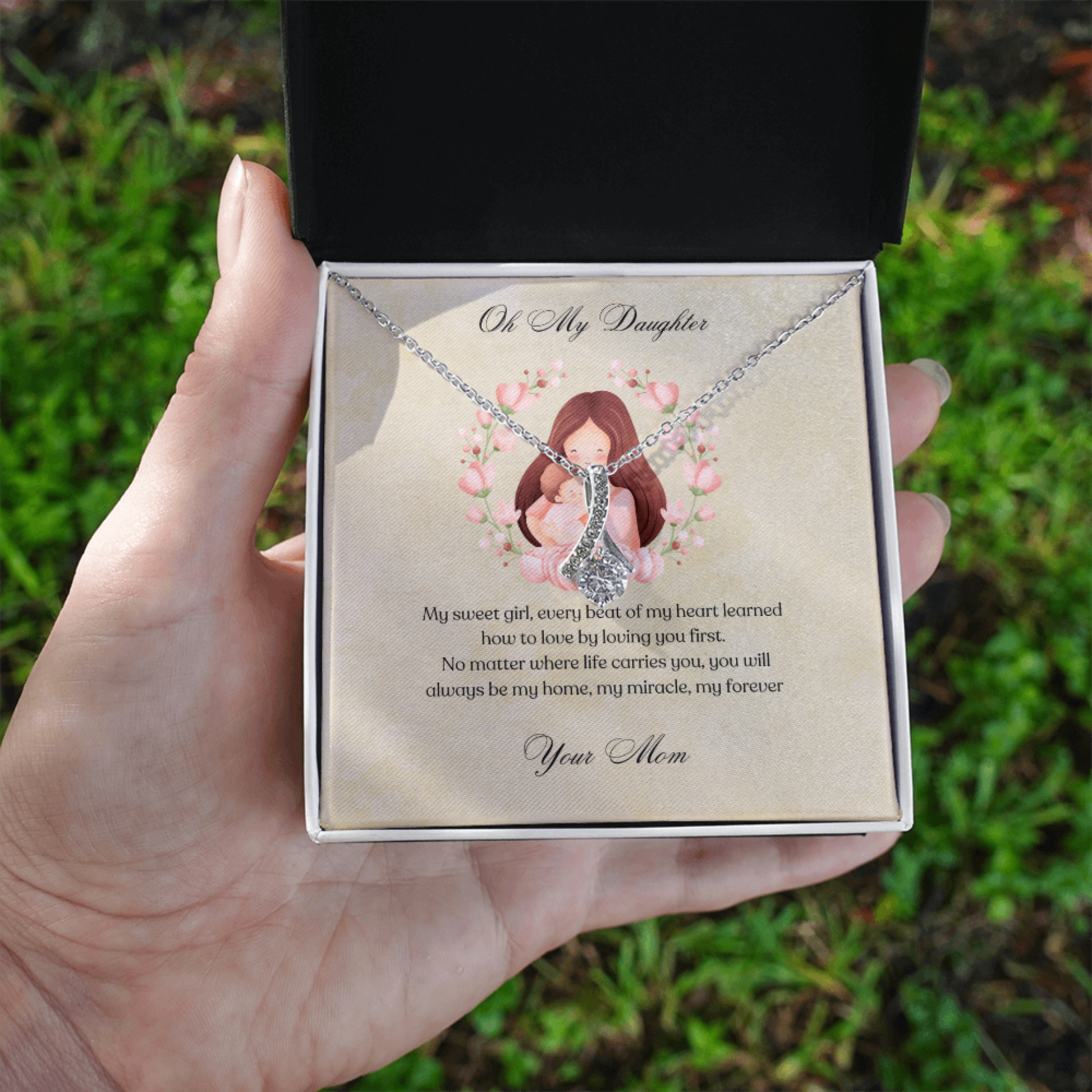 Necklace in a standard box with a sentimental message, held by a hand against a natural background.