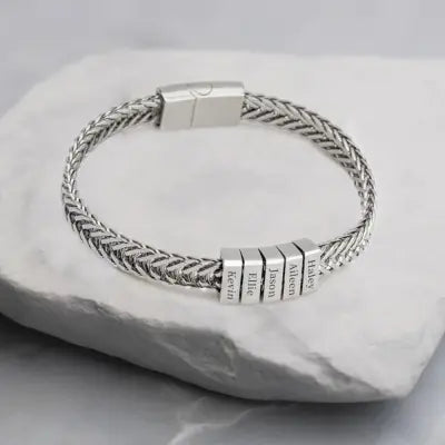Silver braided bracelet with engraved name charms on a light gray stone surface