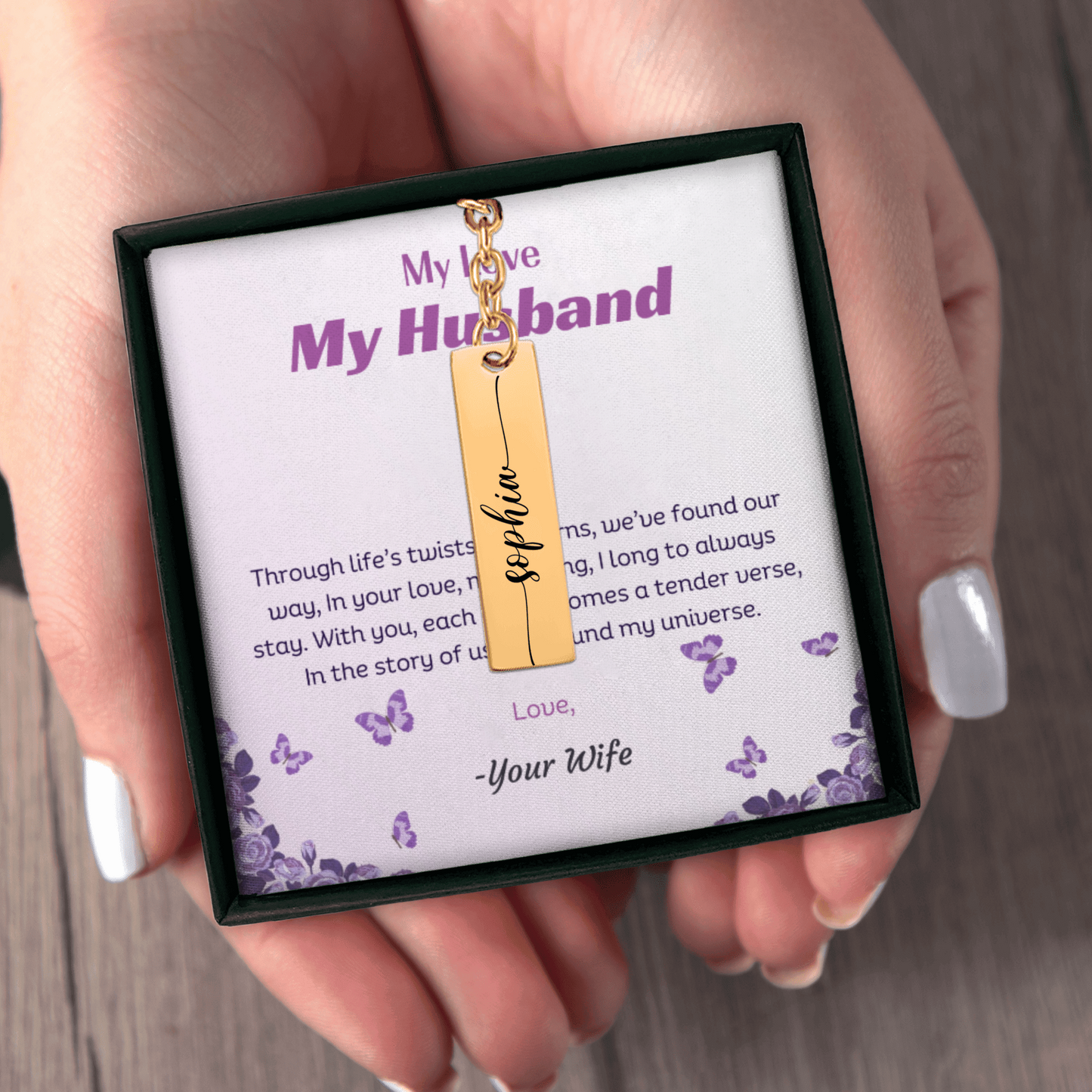 Gold necklace with a tag in a box labeled 'My Love, My Husband' held by a hand.