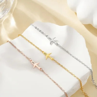Three gold necklaces with customized name on airplane pendants on a white surface.