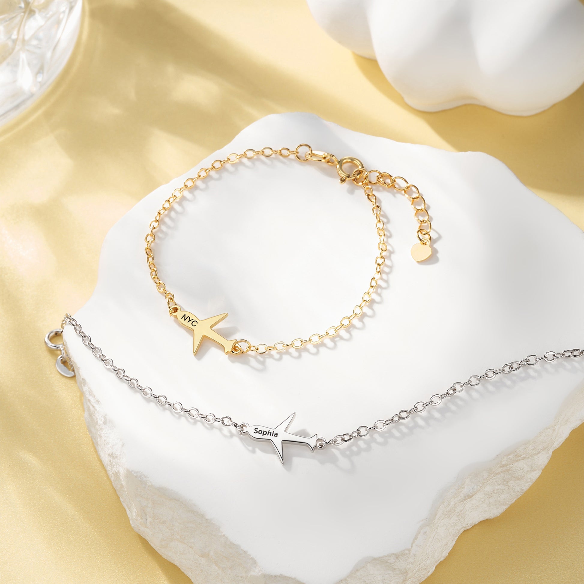 Two gold and silver bracelets with airplane and star designs on a white surface.