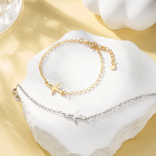 Two gold and silver bracelets with airplane and star designs on a white surface.