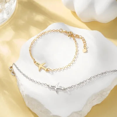 Two gold bracelets airplane charms on a white stone surface.