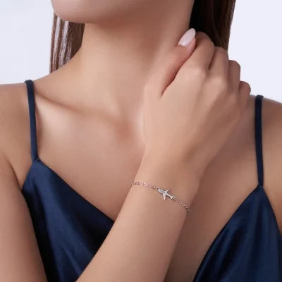 Woman wearing a delicate bracelet with a starfish charm on a plain background