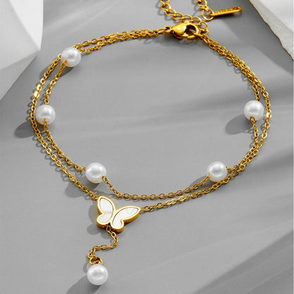 Gold anklet with pearls and a butterfly charm on a gray surface
