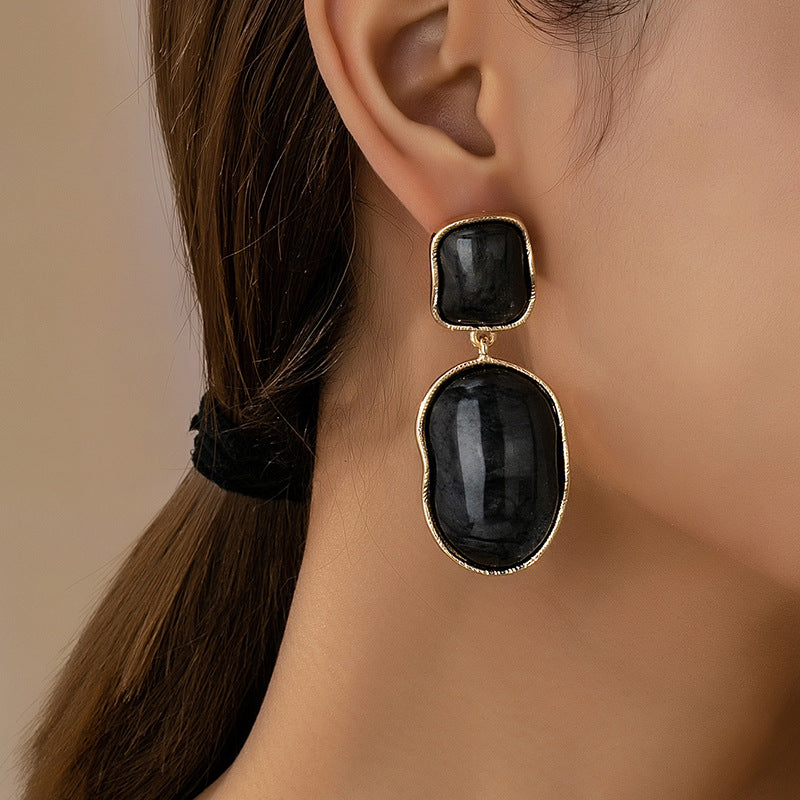 Black earrings with gold accents worn by a person against a neutral background