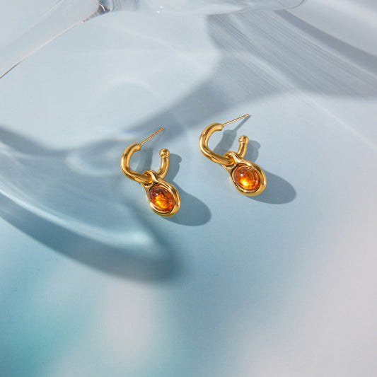 Gold hoop earrings with amber stones on a light blue fabric background