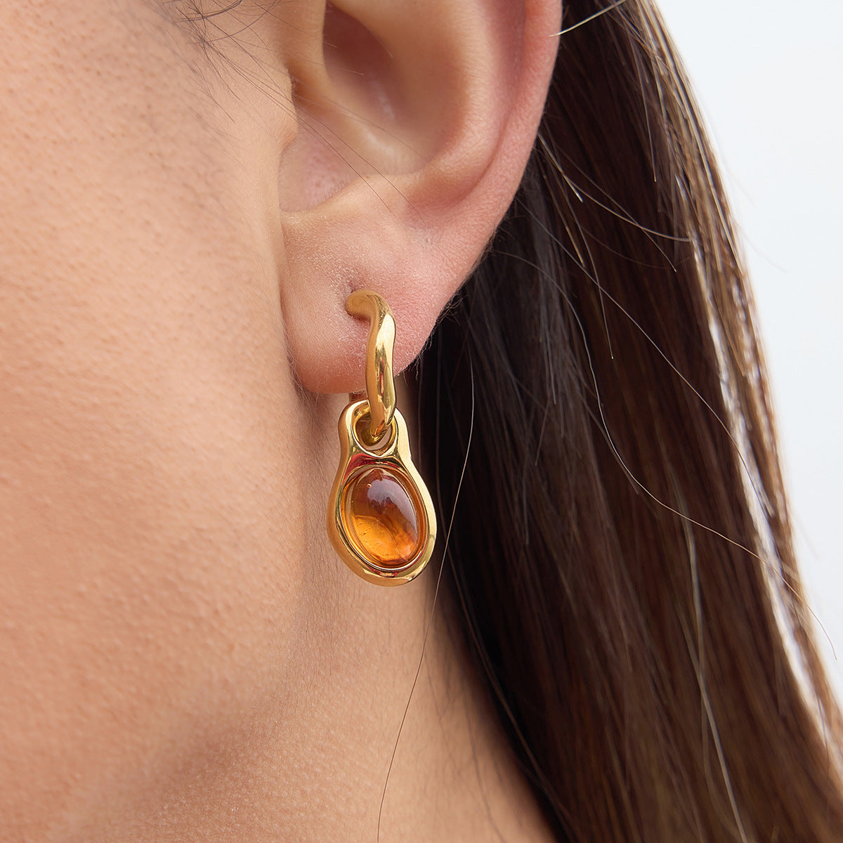 Gold earring with a amber stone worn by a person
