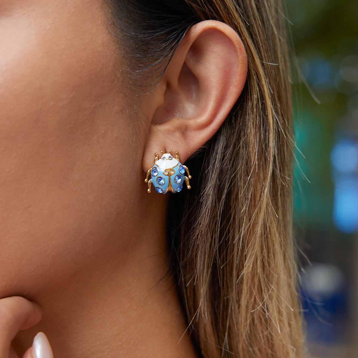 Close-up of an ear wearing a blue and gold earring with blurred background