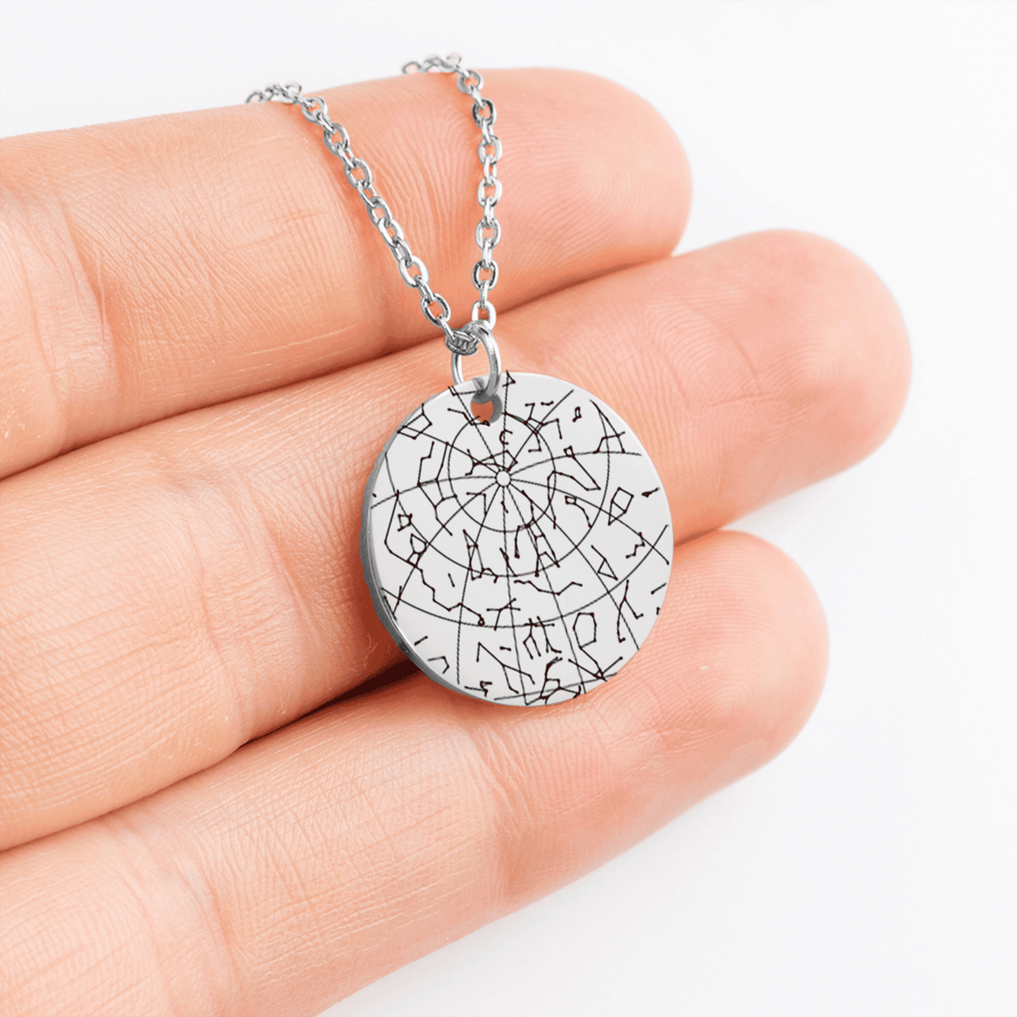 Silver necklace with a round pendant held in a hand against a white background